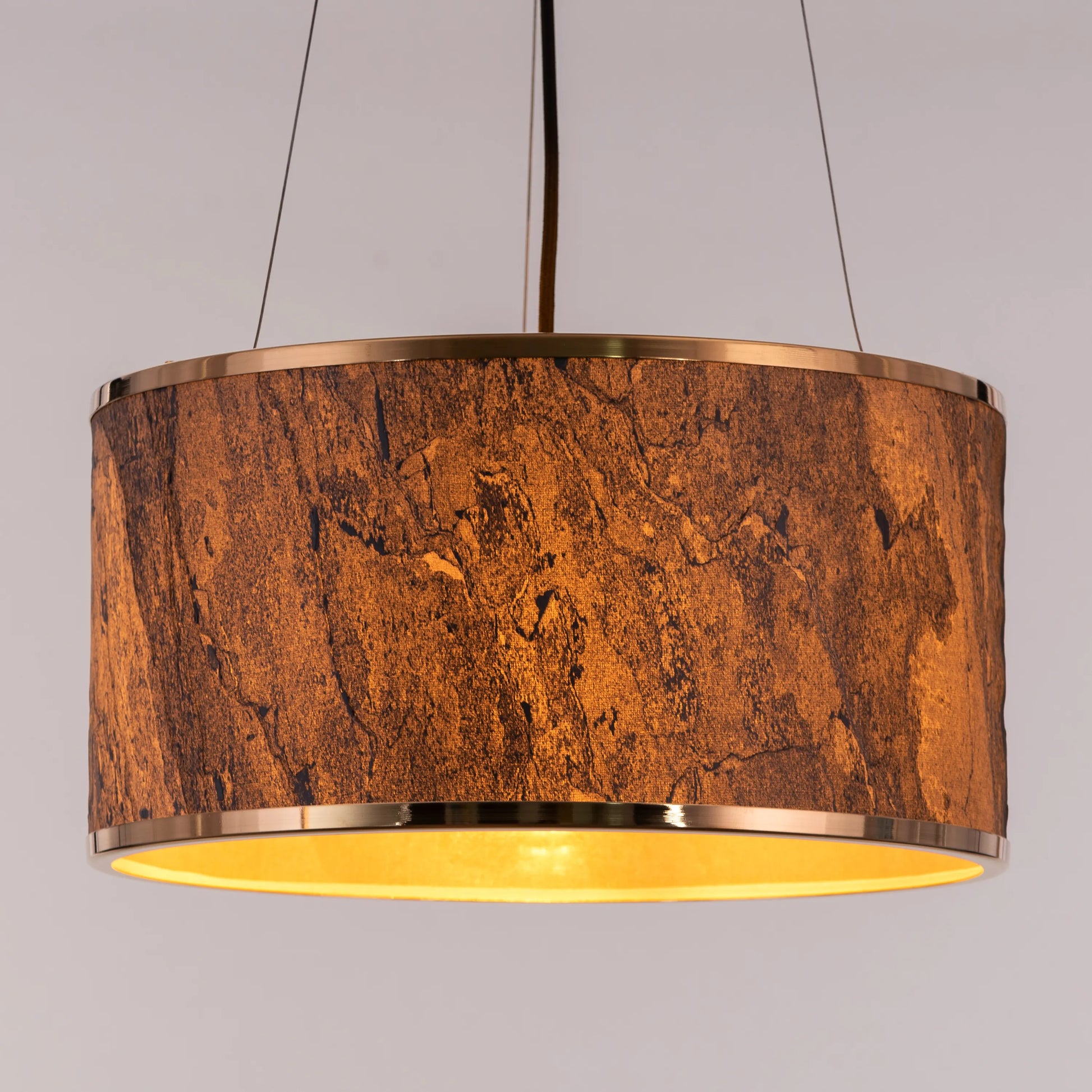 A contemporary pendant light named 'Touch & Glow,' featuring a striking gold stone veneer shade. The light's sleek design showcases the natural texture of the stone, beautifully reflecting and diffusing light to create a warm, inviting ambiance. This pendant light adds a touch of luxury and sophistication, making it an ideal choice for modern interiors.
