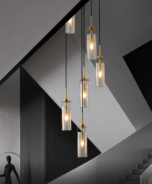 A 6-light brass chandelier with crackle glass globes hangs from the double-height ceiling of a beach villa staircase. The chandelier casts a warm, inviting glow on the space.