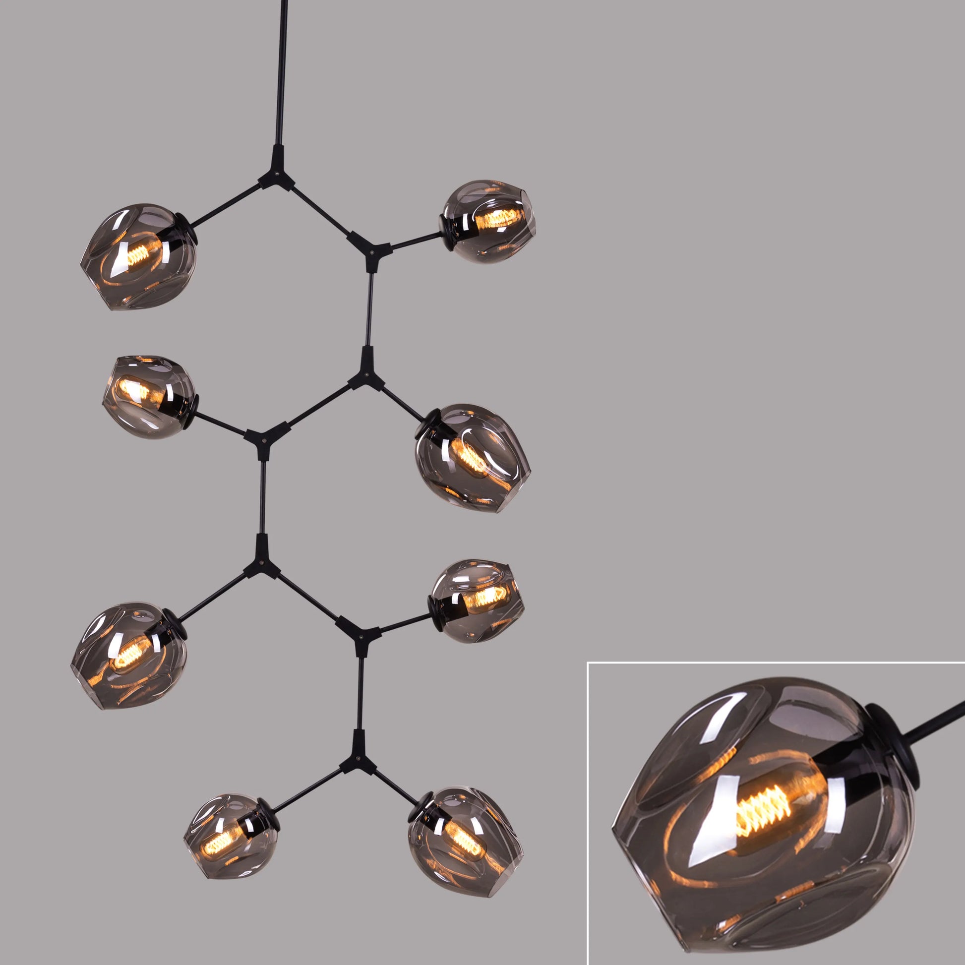 Twist In The Tale 8-head glass chandelier in black and smokey grey, illuminating a modern living room.