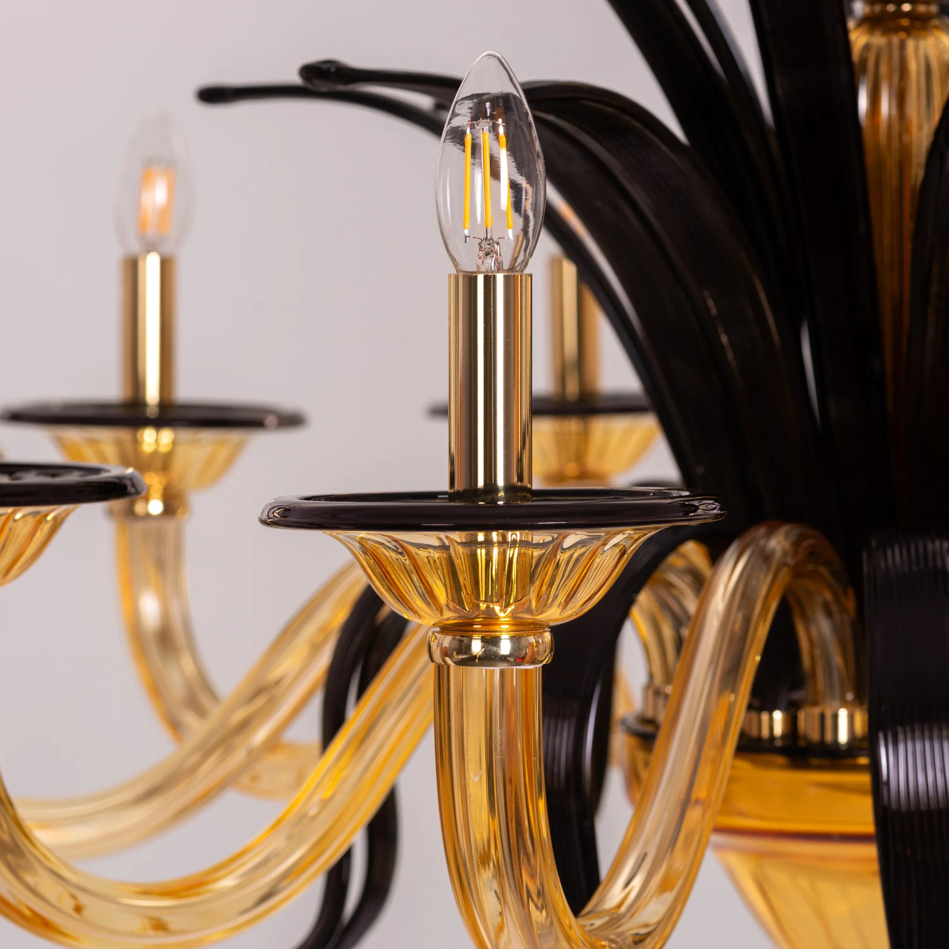 Large "Melodrama" chandelier with amber textured glass and black metal frame, dramatically illuminated in a spacious room.